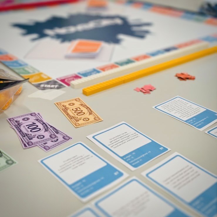 Des cartes Projet bleues et des billets de jeu posés devant le plateau Novacity, avec ses files de briques de couleur.