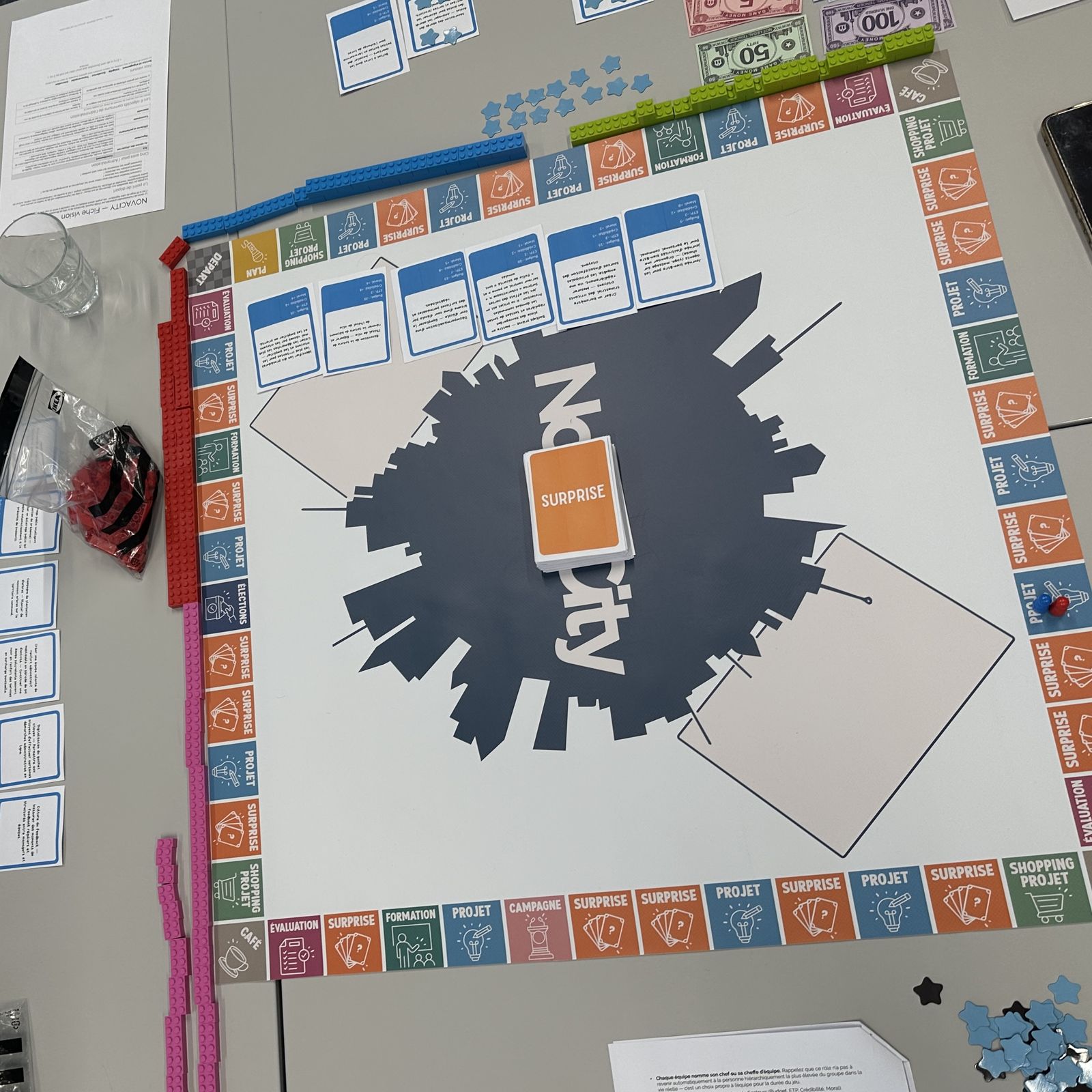 Le plateau Novacity en cours de partie : cases colorées, files de briques de couleur, cartes et jetons.